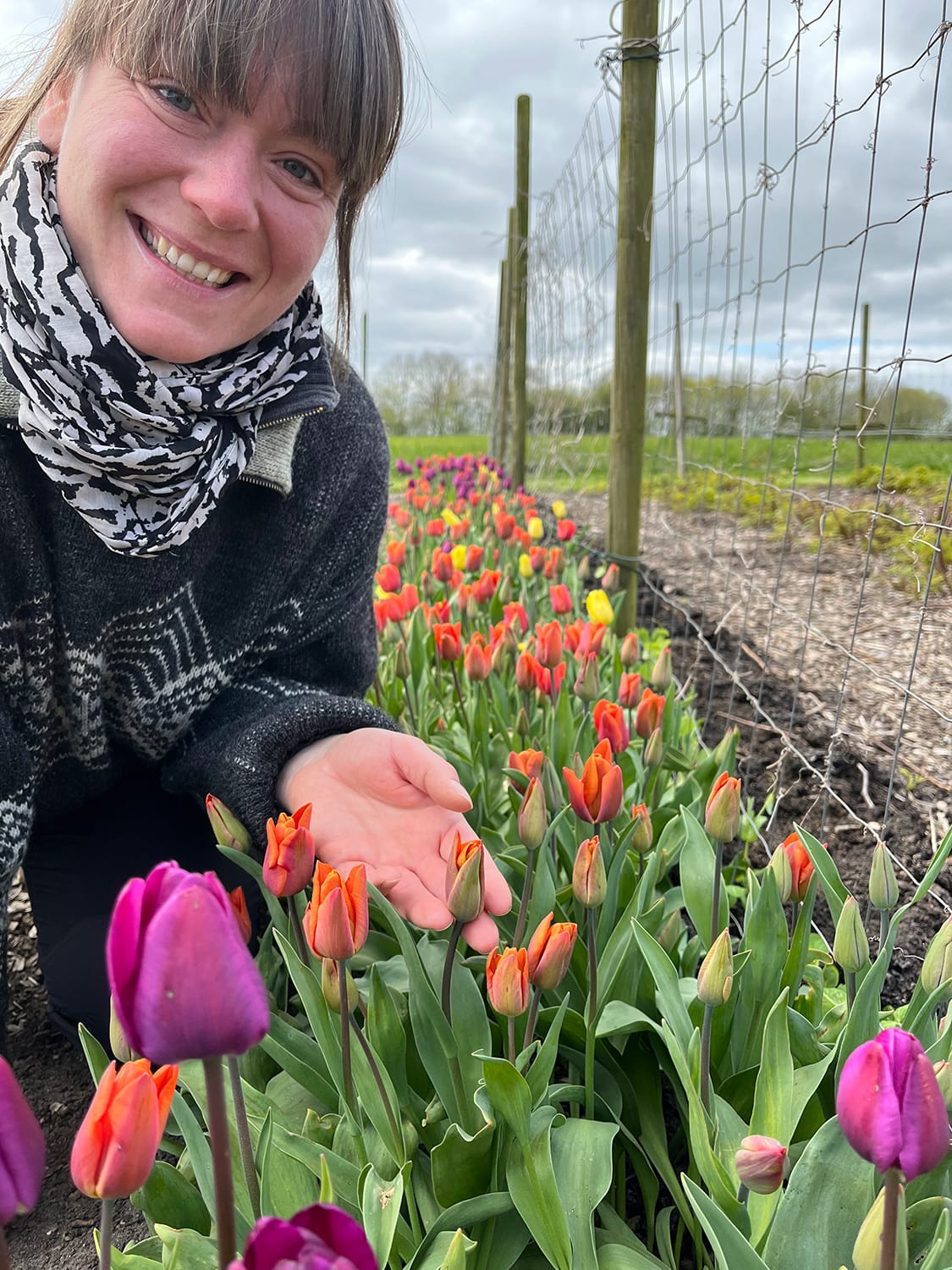 Anne er midt i tulipanrækken i køkkenhaven, mens hun holder en orange tulipan